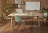 Aarhus Wheelie Chairs by Quell Design in soft morandi green arranged around a rectangular table in a modern office setting with exposed red brick walls and light wooden flooring. These Scandinavian-style ergonomic chairs feature smooth moulded polypropylene seats and black five-star swivel bases with castors, combining mobility, comfort, and minimalist design for collaborative learning environments.