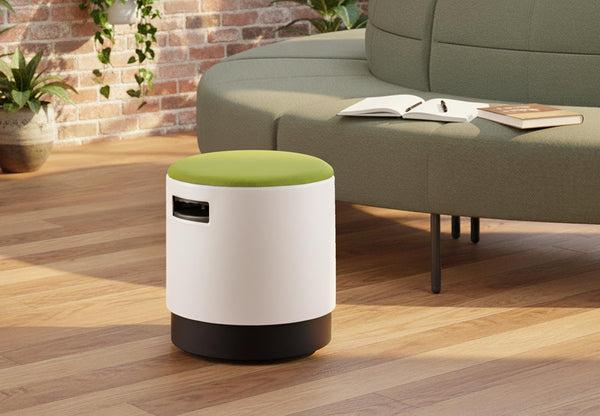 Ikon Rounded Comfort Stool featured in a contemporary office lounge, positioned in front of a Hage circular sofa, with wooden flooring, exposed brick walls and greenery, showcasing modern breakout seating for collaborative and relaxed work environments.
