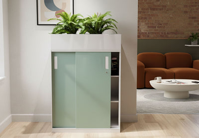 Moda Planter Filing Cabinet in a modern living room setting with exposed brick and white walls and wooden flooring. The cabinet features a powder-coated surface, ABS handles, and a front lock, offering durable, stylish, and practical storage for contemporary residential or office interiors.